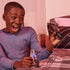 Young boy in a blue long-sleeve shirt smiles widely while playing with DC Spin Master Batman and villain action figures on a neatly made bed with plaid blanket.
