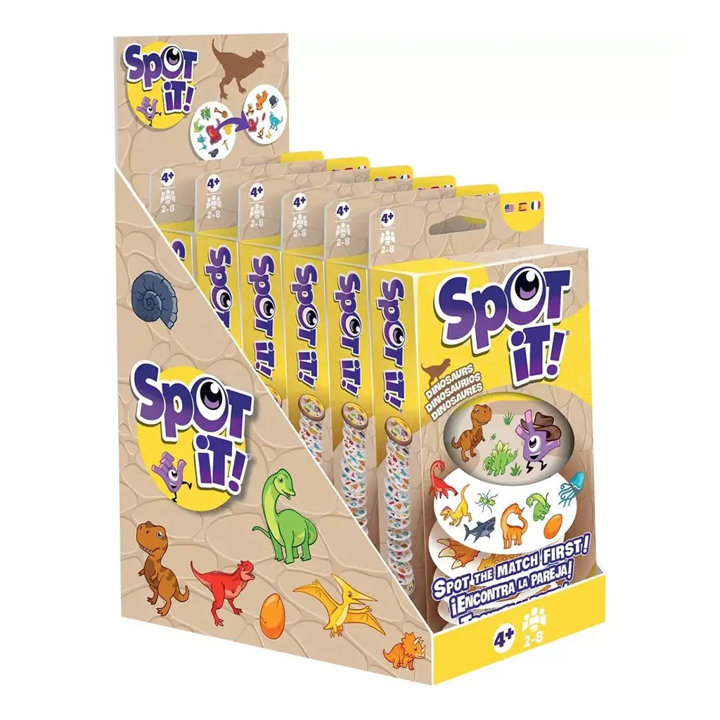 Spot It! Dinosaurs card game retail display features tan and yellow cardboard holding six boxed games, with cartoon dinosaurs, purple logos, and matching-game artwork on white.