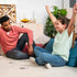 Spot It! Disney card game lifestyle scene shows a man in a coral shirt and a girl in a striped shirt playing with round matching cards on a rug in a bright living room.