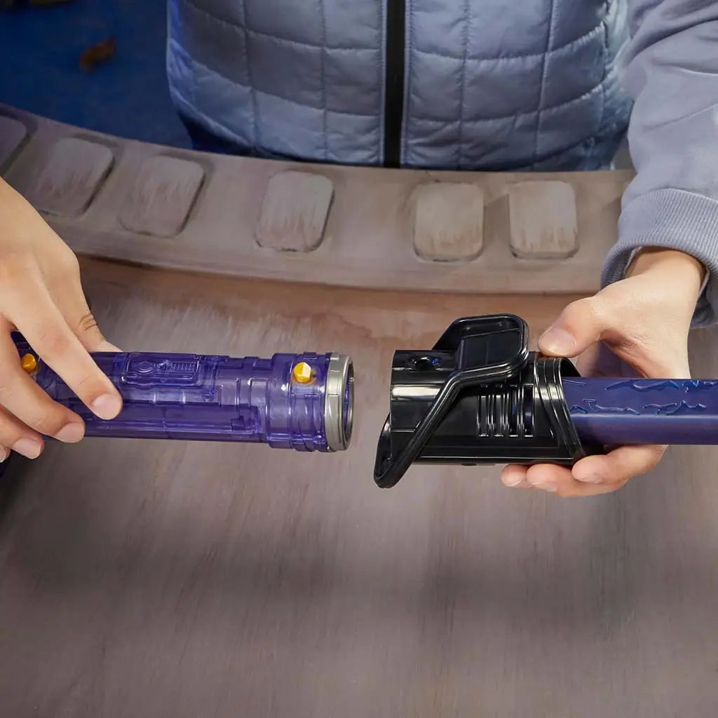 Star Wars Lightsaber Forge components being connected by a child’s hands, showing purple hilt section, black connector, and blue blade part assembled on a wooden table in a playful room setting.