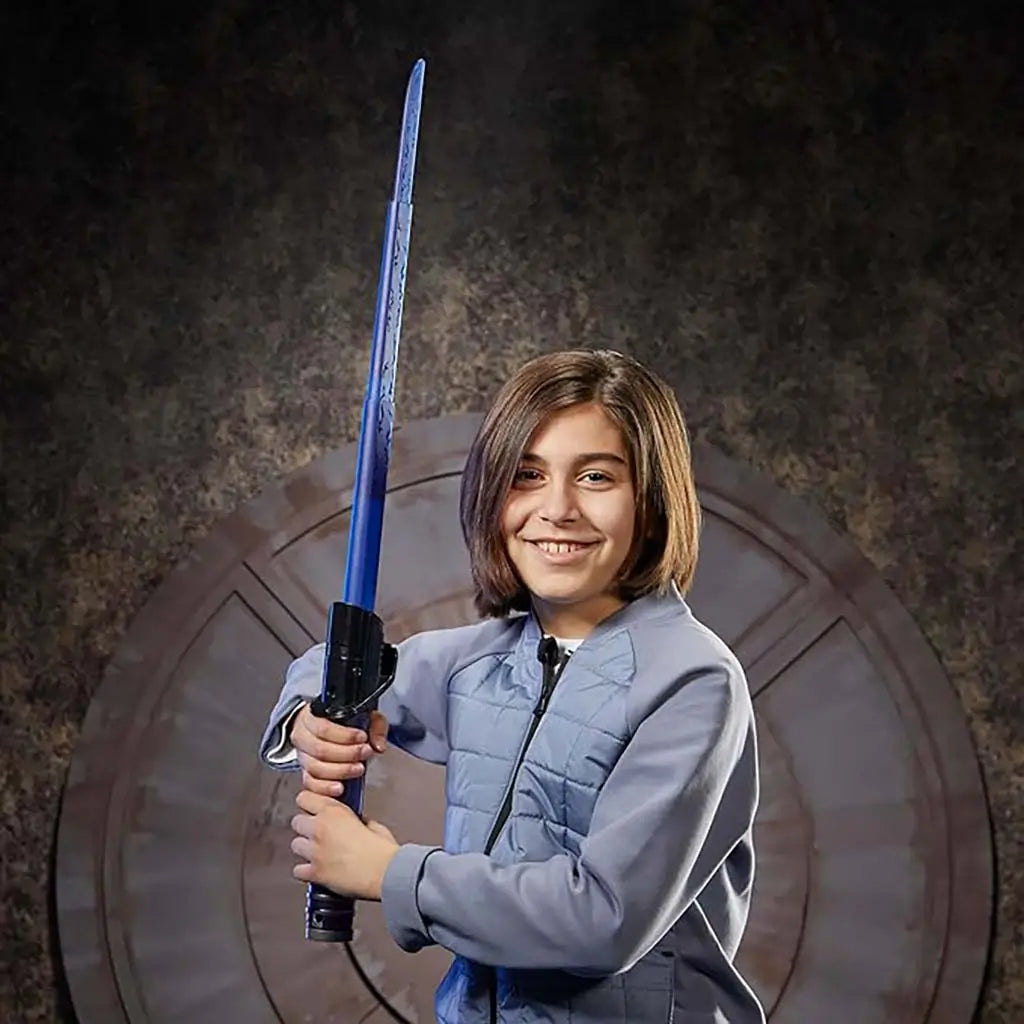 Child holding completed Star Wars Lightsaber Forge blue lightsaber with black hilt, posing confidently in a dim sci-fi themed room with circular wall design that enhances imaginative role-play fun.