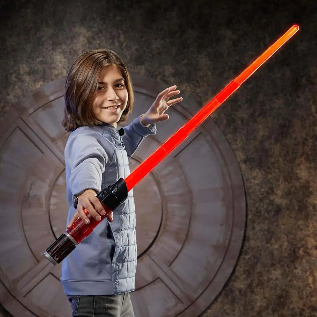 Child posing with completed Star Wars Lightsaber Forge Darth Vader lightsaber, holding the glowing red blade confidently in a dim sci-fi themed room with a circular metallic backdrop.