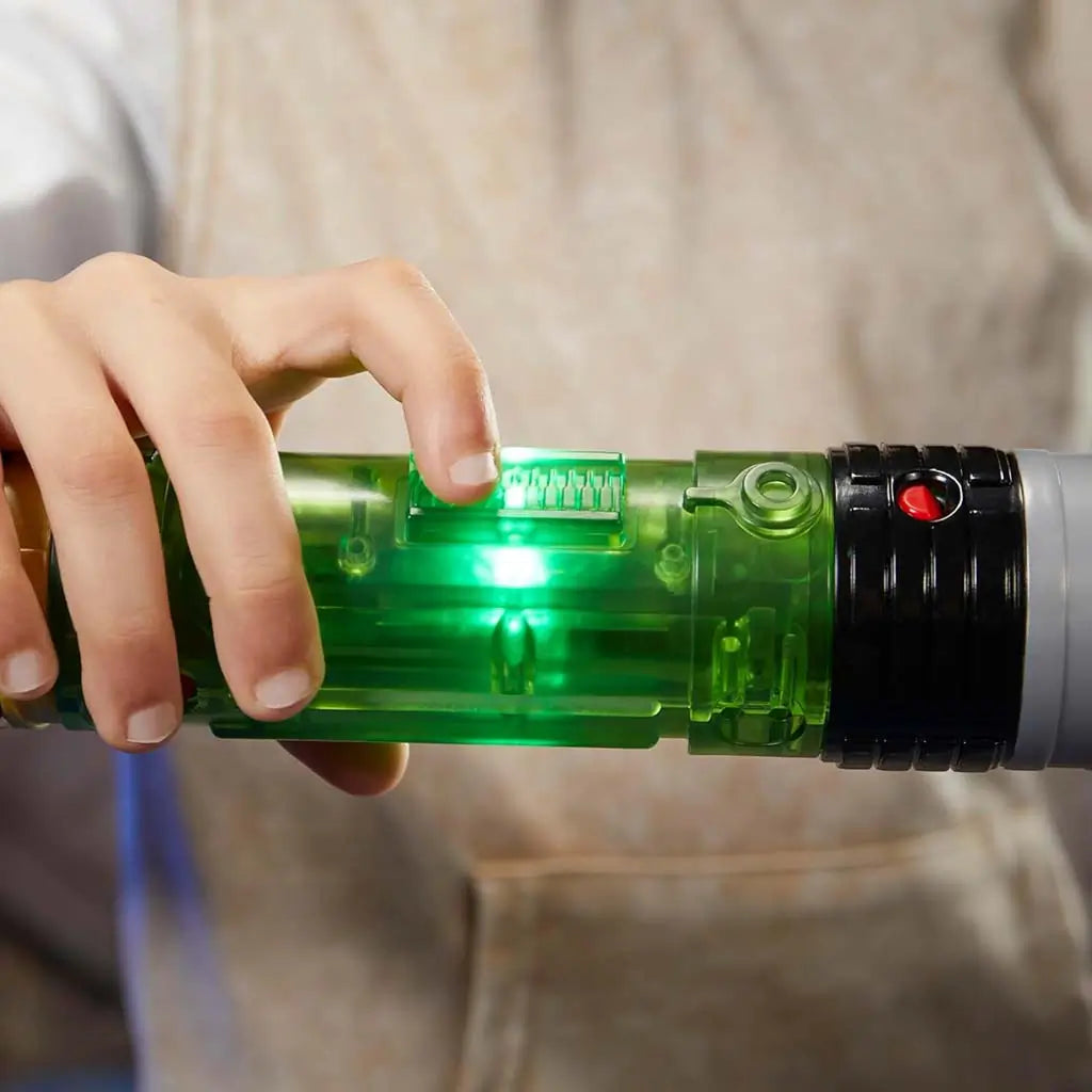 Star Wars Lightsaber Forge Sabine Wren glowing core feature, showing a child’s hand sliding a switch on the translucent green hilt as a bright green light shines from inside against a soft backdrop.