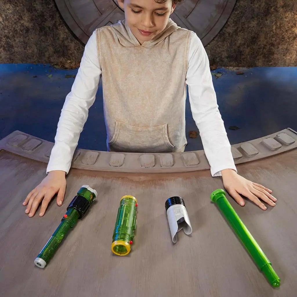 Star Wars Lightsaber Forge Sabine Wren buildable toy parts on a curved wooden table, including green hilt sections, silver emitter shroud, and green blade piece while a child assembles them.