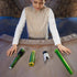 Star Wars Lightsaber Forge Sabine Wren buildable toy parts on a curved wooden table, including green hilt sections, silver emitter shroud, and green blade piece while a child assembles them.