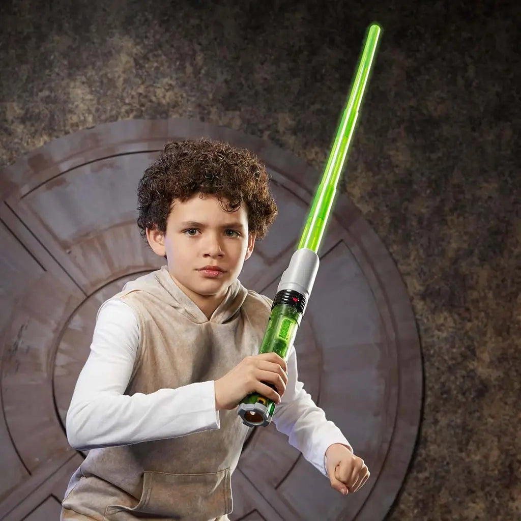 Child posing ready with Star Wars Lightsaber Forge Sabine Wren green lightsaber, gripping the silver and green hilt and extending the glowing blade in a sci-fi themed room with circular wall design.