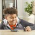 Smiling child in an orange shirt and gray jacket playing with Star Wars Mission Fleet Mandalorian figure and hover E-Web cannon on a wooden table in a cozy, well-lit living room.