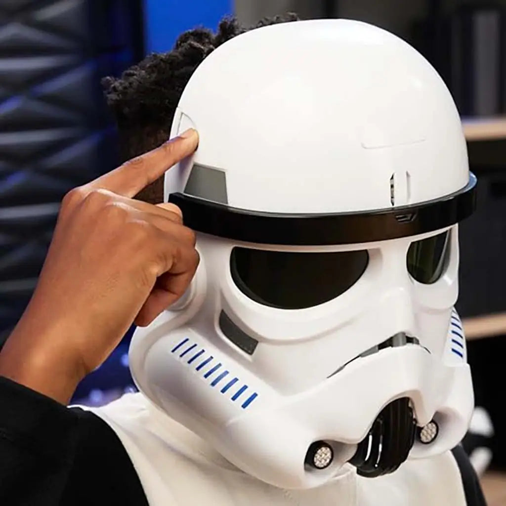 Star Wars Stormtrooper white electronic helmet worn by child who presses side button to activate sounds, showing smooth curved shell and black visor band in playful indoor setting