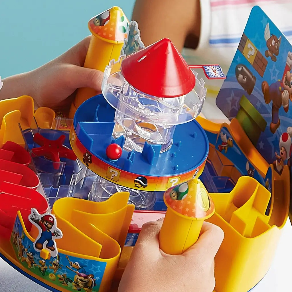 Close-up view of Super Mario Castle Land game shows a child’s hands guiding a red ball through maze paths and obstacles, with Mario-themed towers, traps, and colorful castle details.