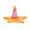 Super Mario Galaxy Movie Princess Peach figure wears a pink gown, white gloves and gold crown, posed with raised arms on a glossy orange-gold star platform against white.
