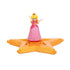 Super Mario Galaxy Movie Princess Peach figure wears a pink gown, white gloves and gold crown, posed with raised arms on a glossy orange-gold star platform against white.
