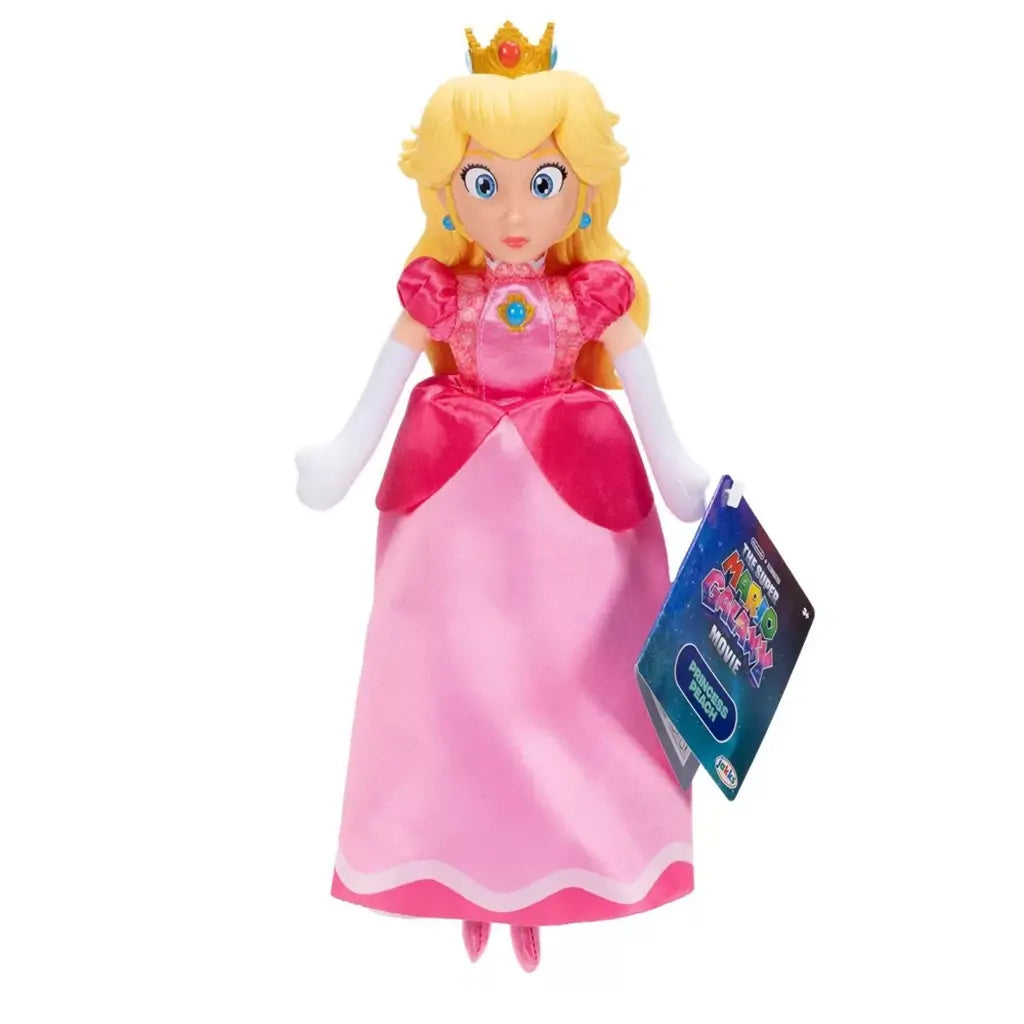 Princess Peach plush toy from The Super Mario Galaxy Movie features soft pink satin dress, blonde hair, gold crown, white gloves, blue jewelry, and retail tag on white.