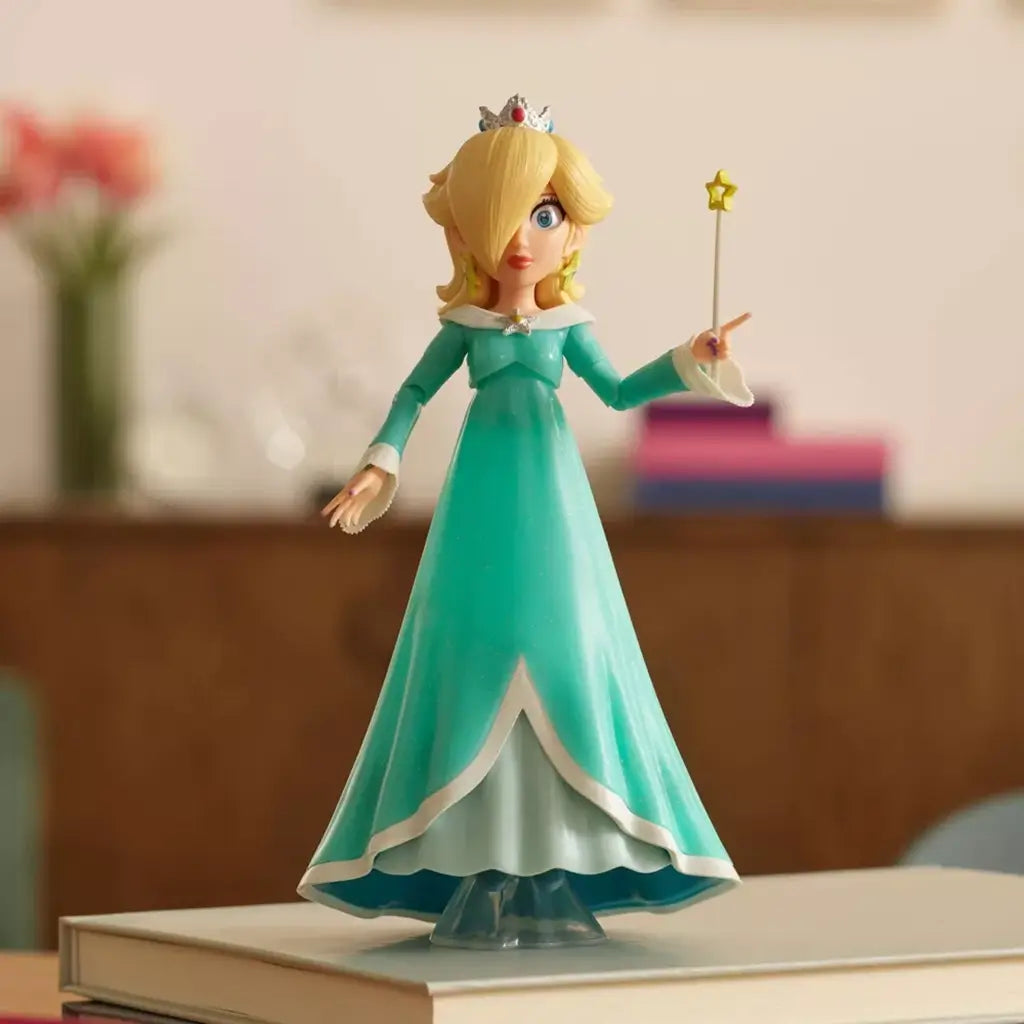 Super Mario Galaxy Movie Rosalina figure wears a turquoise plastic gown with white trim and silver crown, holding a yellow star wand while displayed on stacked books.