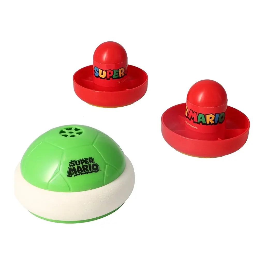 Close-up of Super Mario Hover Shell Strike game pieces including a green shell puck with logo and two red strikers labeled “SUPER MARIO” on a plain background.