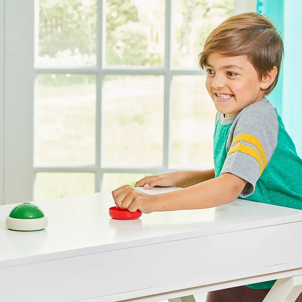 Child smiling while playing Super Mario Hover Shell Strike game, using a red striker on a white table with a green shell puck gliding across in a bright room.