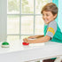 Child smiling while playing Super Mario Hover Shell Strike game, using a red striker on a white table with a green shell puck gliding across in a bright room.