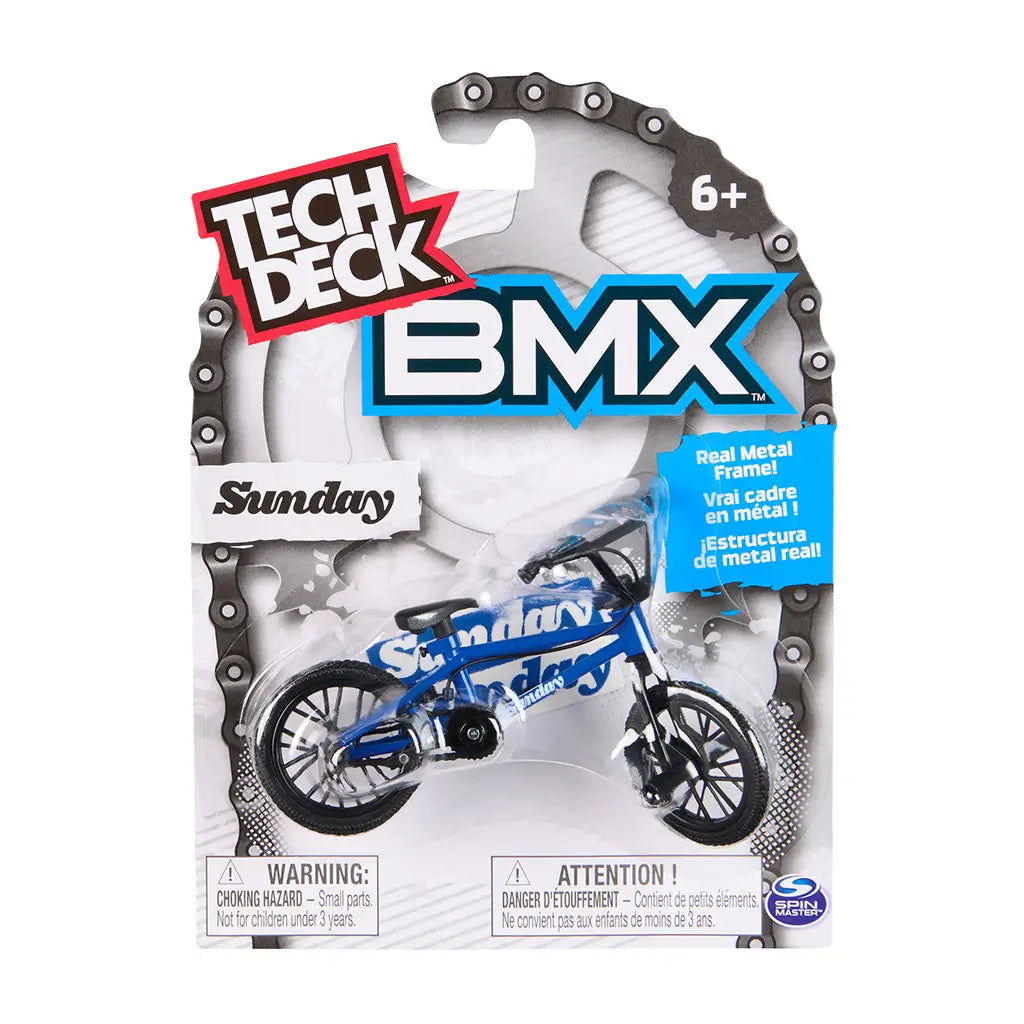 Tech Deck BMX toy packaging in white cardboard with gray chain graphic border and clear plastic blister, displaying blue Sunday BMX bike, bold branding, age label, and safety warnings on a clean background.