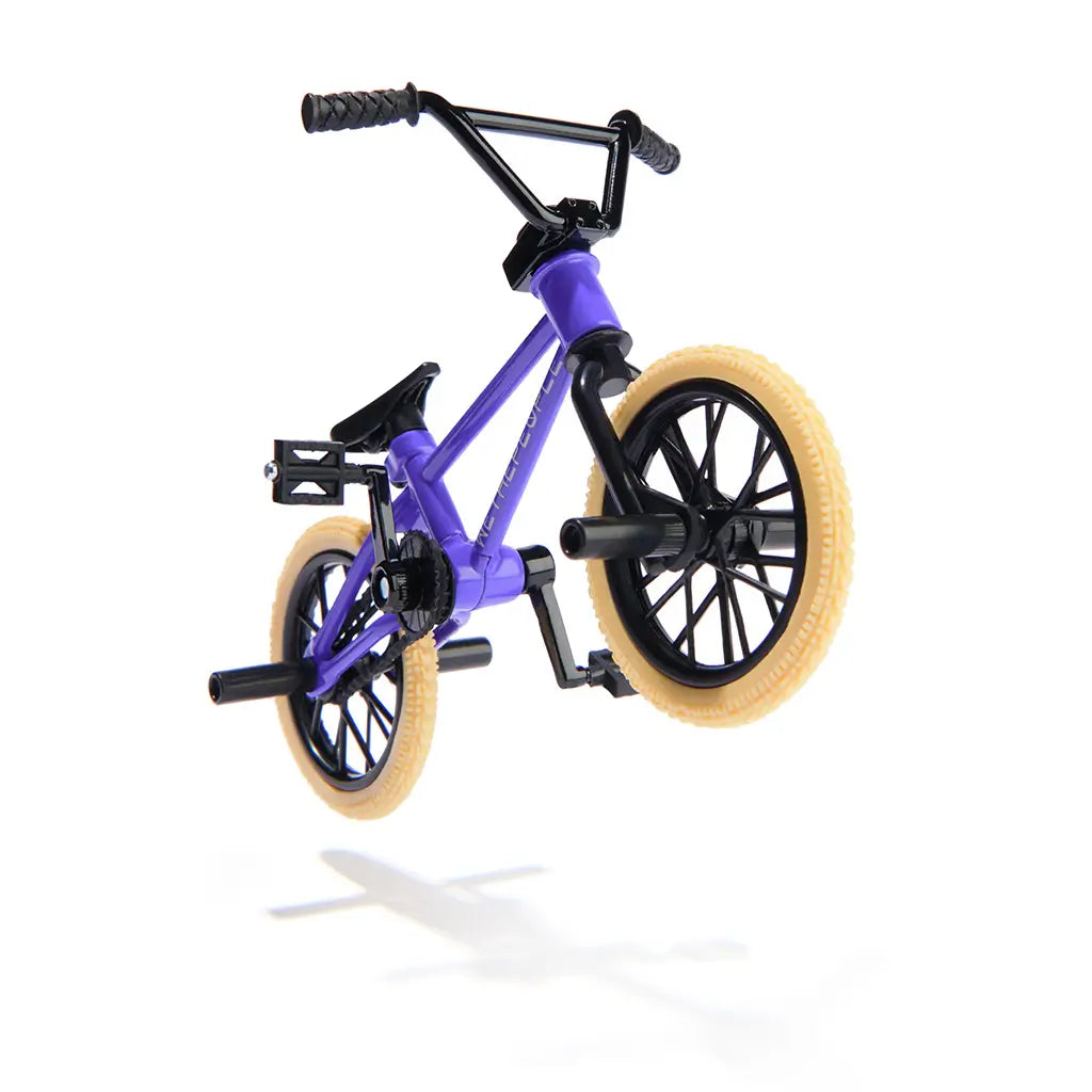 Tech Deck BMX finger bike in purple and black metal and plastic with tan rubber tires, compact stunt frame with pegs and spoked wheels, shown midair against a minimal white studio background.
