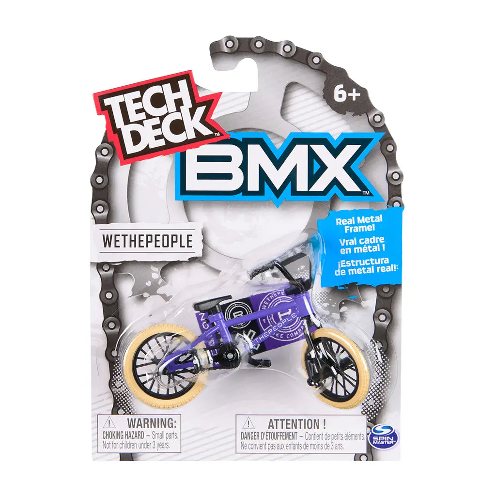 Tech Deck BMX toy packaging featuring purple WeThePeople bike with tan tires, encased in clear plastic on white cardboard with chain graphic border, branding, age label, and safety warnings.