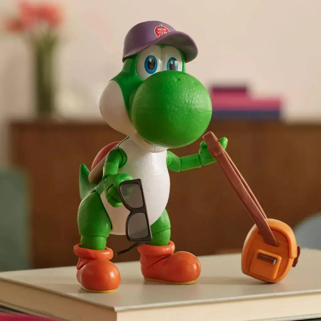 Super Mario Galaxy Yoshi figure in green plastic with soft texture, rounded character form wearing purple cap and holding accessories, displayed on tabletop setting with blurred indoor background