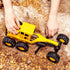 Hands playing with yellow Tonka grader toy on sandy, rocky terrain, showcasing the toy’s rugged tires and durable build for outdoor play.