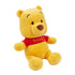 Disney Winnie the Pooh plush toy in soft golden yellow fabric with rounded bear shape, shown at an angled view with a red Pooh shirt, small ears, embroidered eyes and nose, on a white background.