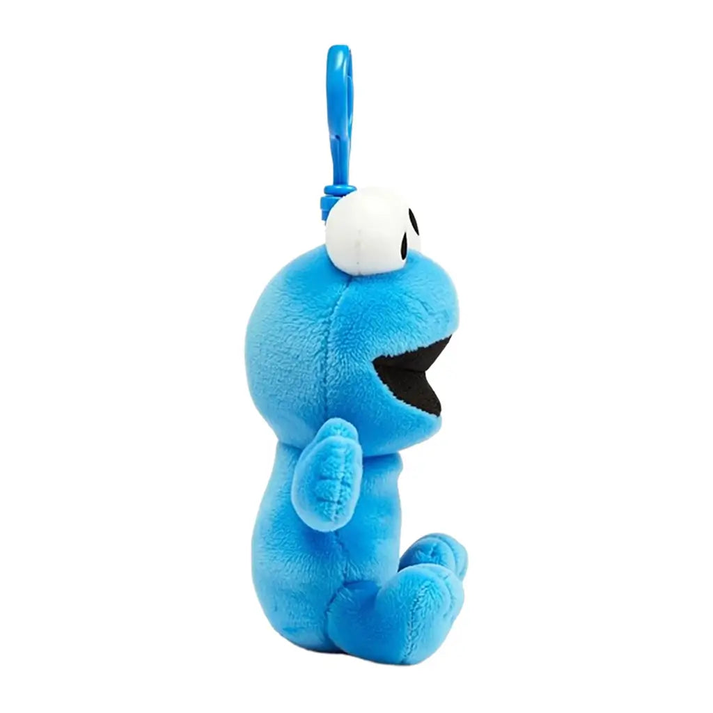 Sesame Street Cookie Monster plush clip in bright blue fuzzy fabric, with large white eyes, black open mouth and seated form, shown in side view with a blue plastic hook on white.