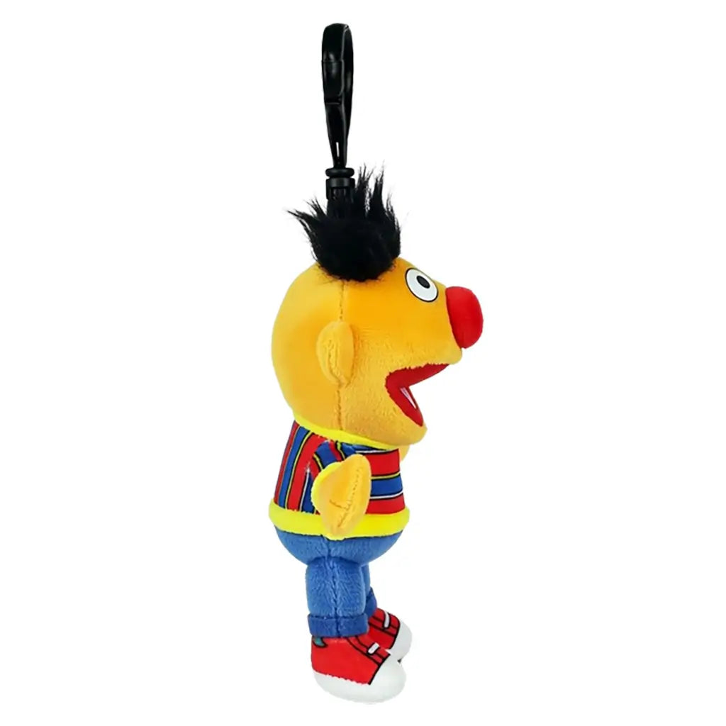 Sesame Street Ernie plush clip in yellow soft fabric, with black hair, red nose, striped shirt, blue pants and red shoes, shown in side view with a black hook on white.