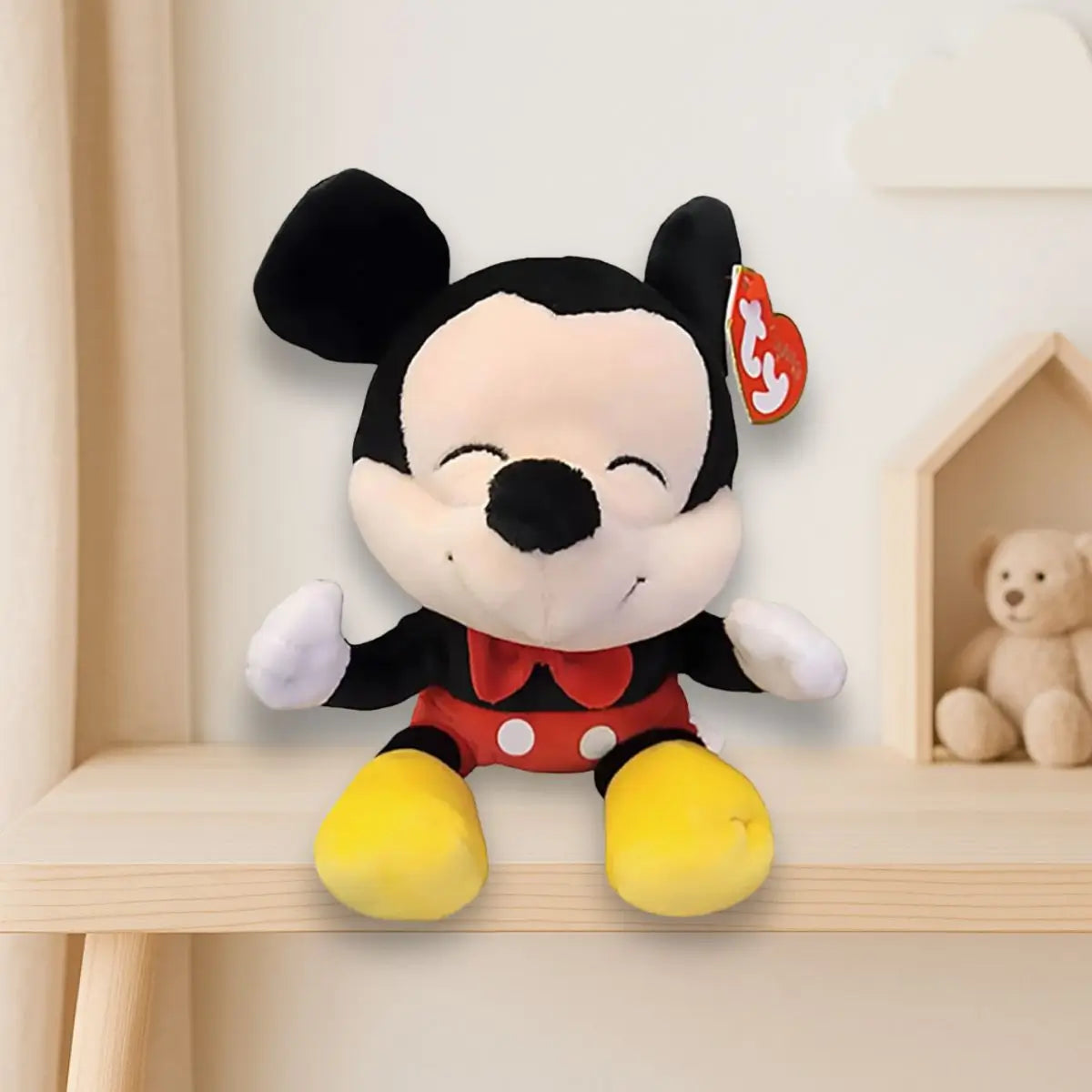 A smiling TY plush Mickey Mouse with closed eyes sits on a light wooden shelf in a cozy nursery setting, with a teddy bear in a small house-shaped shelf and a cloud wall decoration in the background.