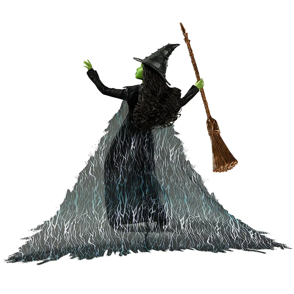 Wicked Elphaba Thropp fashion doll rear view shows long flowing black and green cape with sheer patterned texture, layered skirt construction, and articulated limbs, revealing costume detailing and dramatic silhouette from the back.