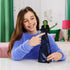 Wicked Elphaba singing doll shown in a lifestyle play scene with a smiling child, green-skinned doll in patterned gown held upright, illustrating interactive singing play in a bright bedroom setting.