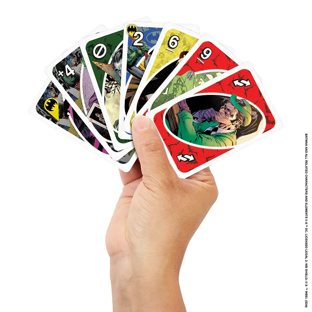 Batman UNO cards featuring colorful comic art of villains like the Joker, Riddler, and Poison Ivy, held in a fan shape by a hand against a white background.