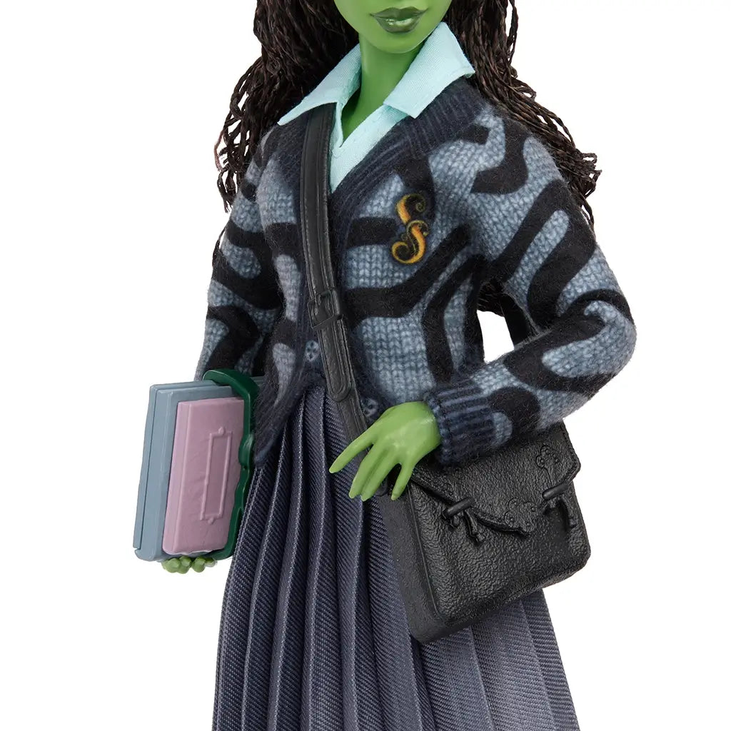 Detailed close-up of Wicked Elphaba doll's torso, featuring a gray patterned knit cardigan with embroidered S emblem, pleated skirt, and shoulder bag strap.