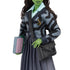 Detailed close-up of Wicked Elphaba doll's torso, featuring a gray patterned knit cardigan with embroidered S emblem, pleated skirt, and shoulder bag strap.