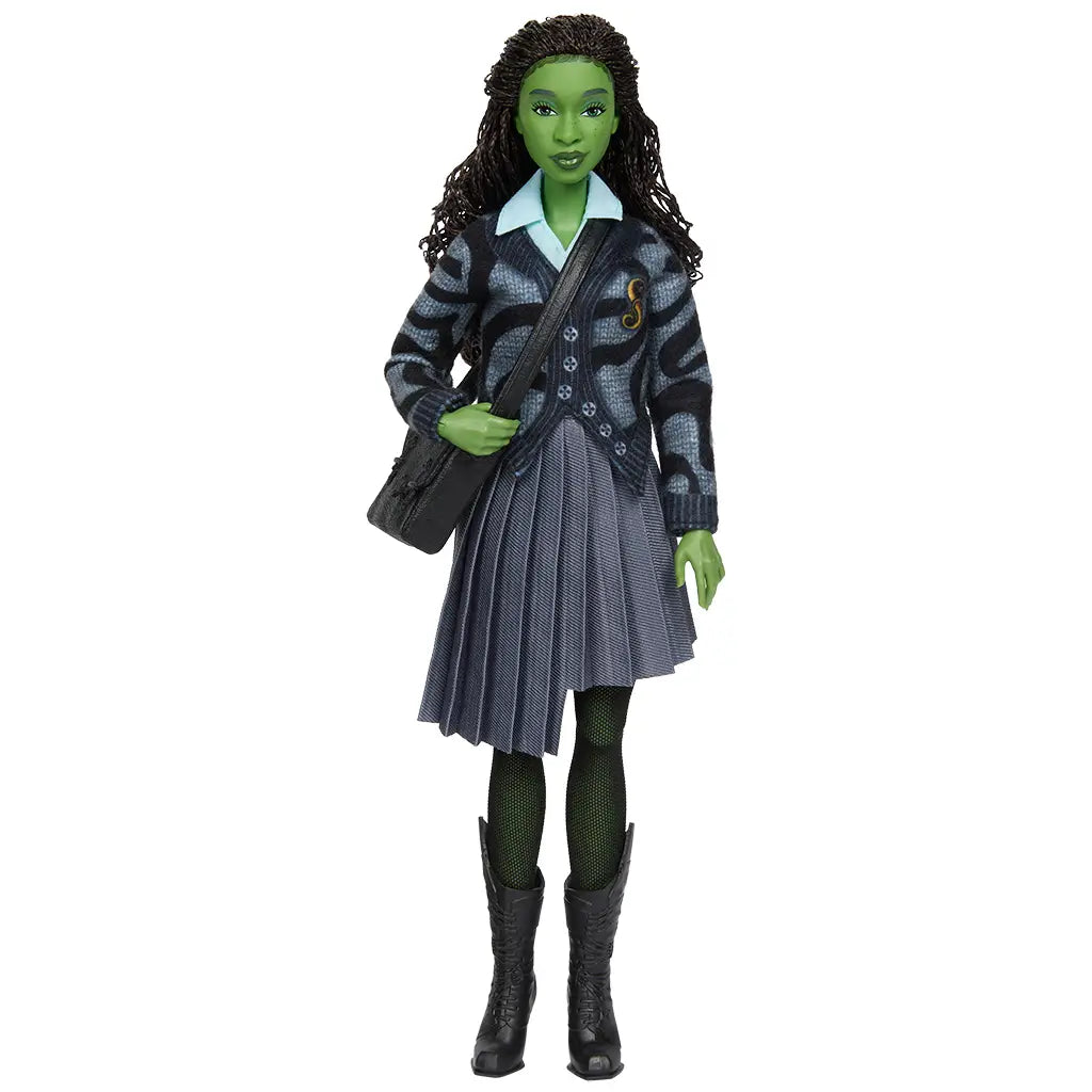 Full front view of Wicked Elphaba doll wearing gray pleated skirt, patterned cardigan, black boots, and black shoulder bag against plain background.
