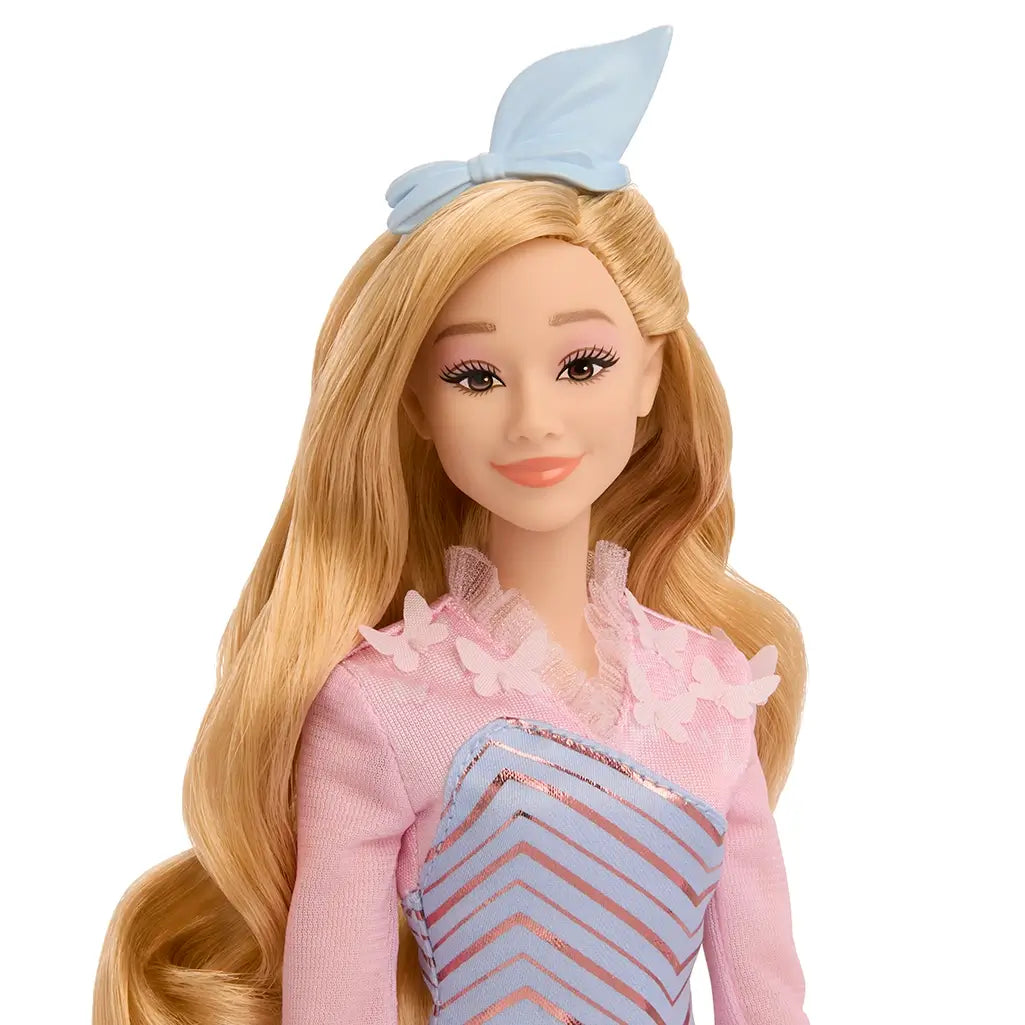 Close-up of Wicked Glinda doll’s smiling face with long blonde hair, pink sheer collar with floral accents, and blue bow headband.