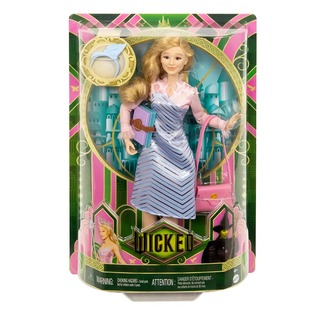 Retail display of Wicked Glinda doll in green and pink Wicked box, holding pastel book and pink bag, wearing blue chevron dress and pink top.