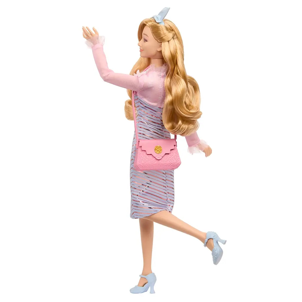 Side view of Wicked Glinda doll waving, showing long wavy blonde hair, pink purse, and light blue chevron dress with metallic accents.