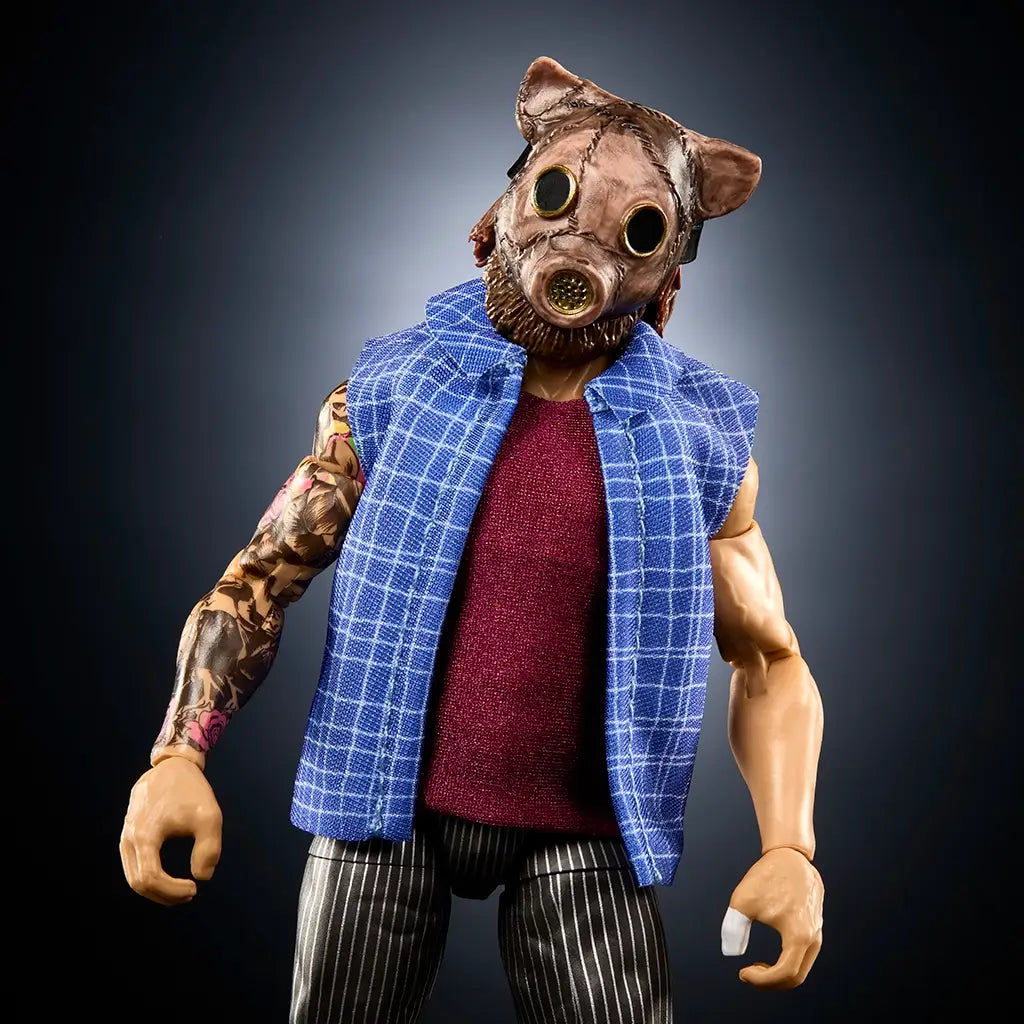 WWE Joe Gacy action figure close-up with tan glossy plastic skin, textured pig mask featuring circular eye lenses, muscular upper body sculpt, blue plaid vest, and maroon shirt, photographed against a dark gradient studio backdrop.