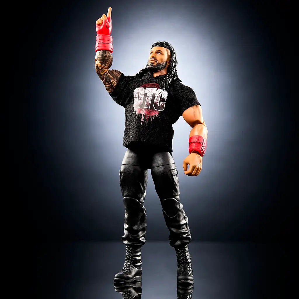 WWE Elite Collection Roman Reigns wrestling figure demonstrating 25 points of articulation, featuring tan and black plastic body, tattooed torso and arms, red glove accessories, black boots, and raised victory pose against a dark studio backdrop.
