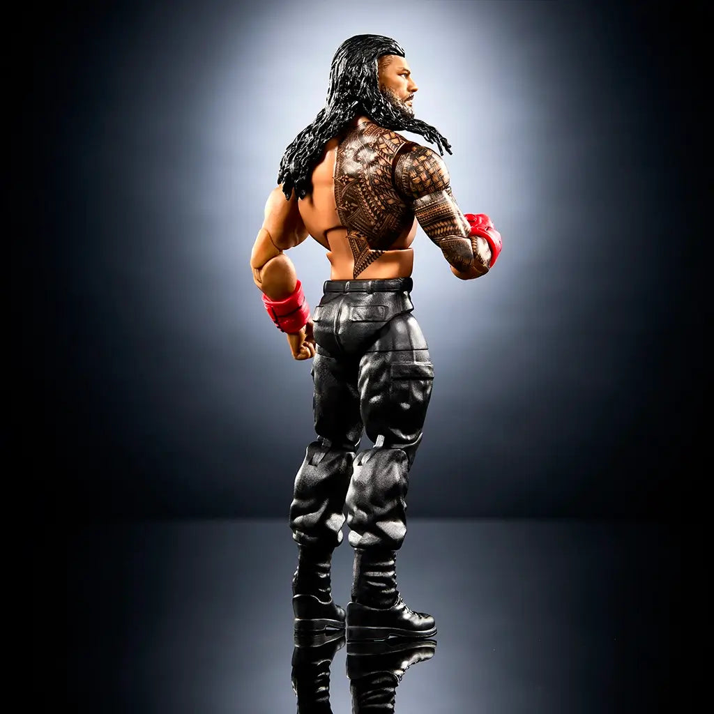 WWE Elite Collection Roman Reigns wrestling figure rear angled view featuring tan and black plastic body, sculpted back muscles, full Samoan-style tattoo coverage, long molded hair, articulated limbs, and black boots against a dark backdrop.