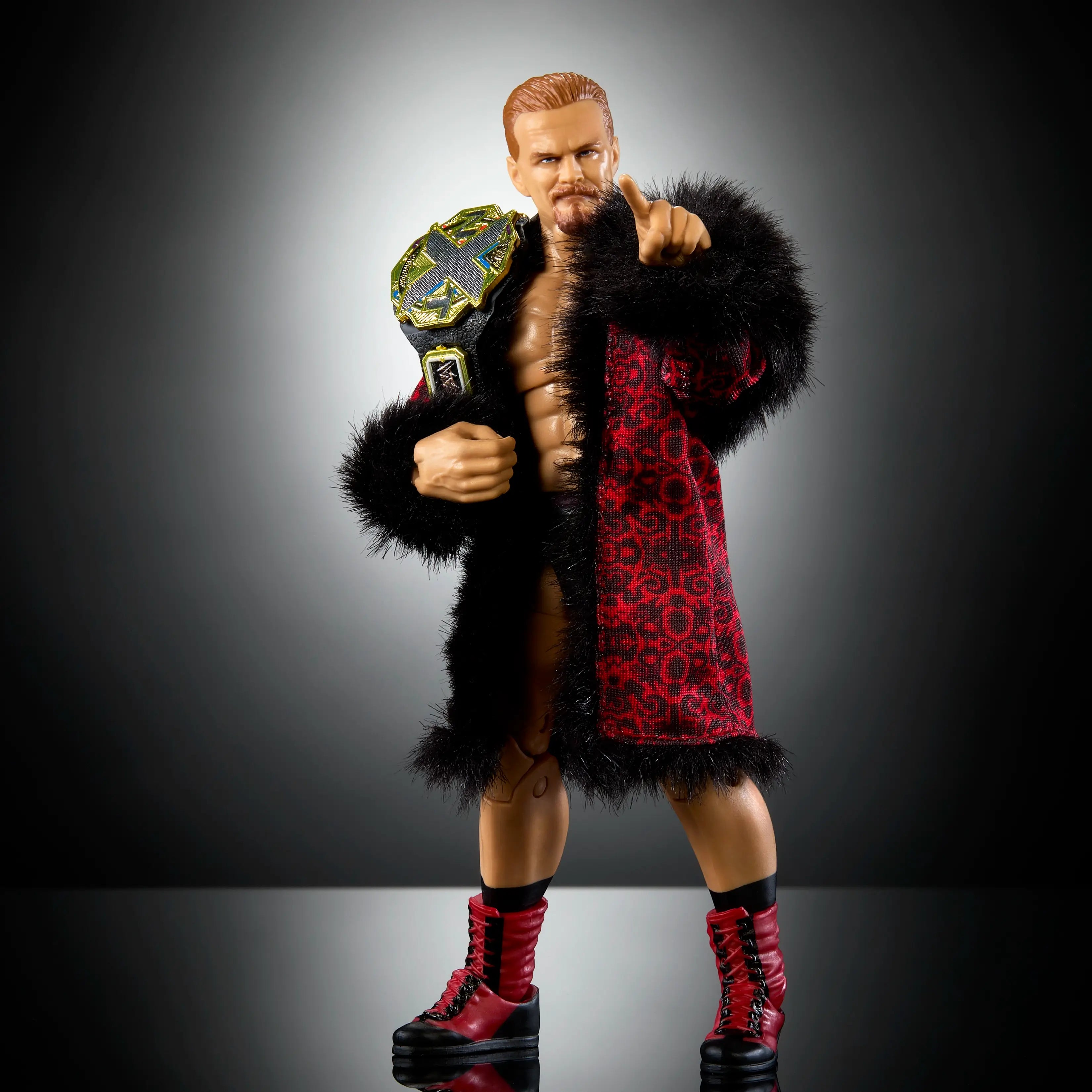 WWE Elite Collection Ilja Dragunov action figure in red patterned robe with black fur trim, holding gold NXT championship belt, posed against dark studio background.