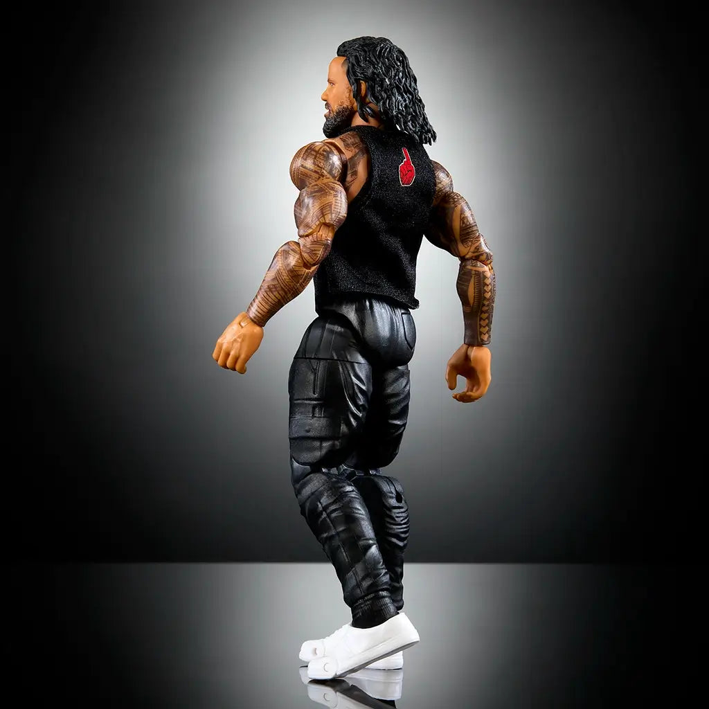 WWE Elite Jimmy Uso action figure rear angled view features black pants, sculpted tattoos, white sneakers, and a sleeveless vest with red logo against dark background.