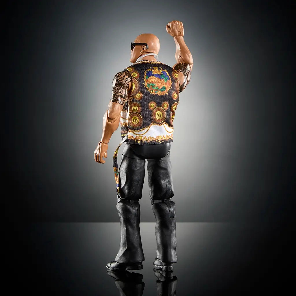 Rear angled view of WWE The Rock action figure in ornate black and gold vest, raising fist with detailed tattoos and black pants against a dark background.