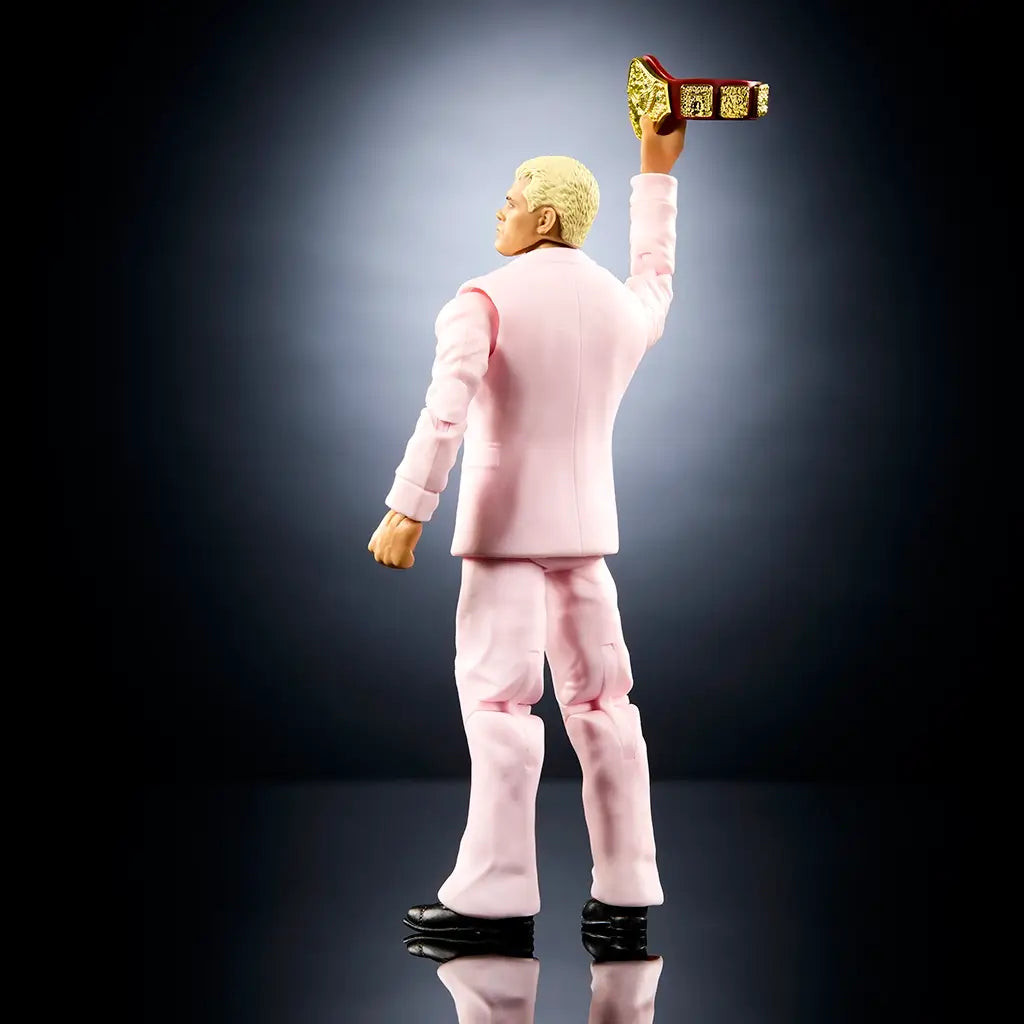 Rear angled view of WWE Cody Rhodes action figure showing fitted pink suit jacket and pants, clean seam sculpting, blond hair detail, raised championship belt accessory, articulated stance, and balanced posture against a dark reflective background.