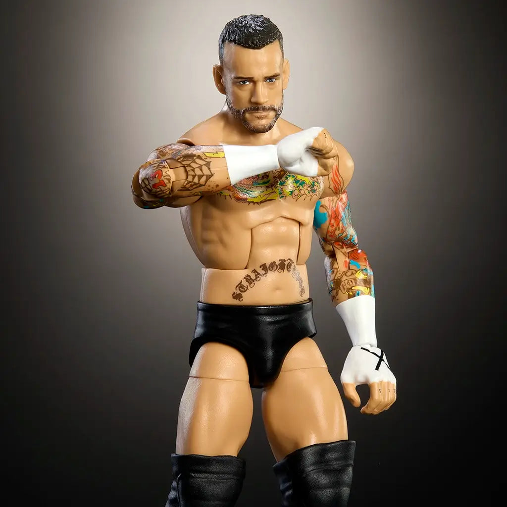 Close-up of WWE Elite CM Punk action figure showcasing muscular torso, colorful tattoos, taped fists with X markings, and realistic sculpt under studio lighting.
