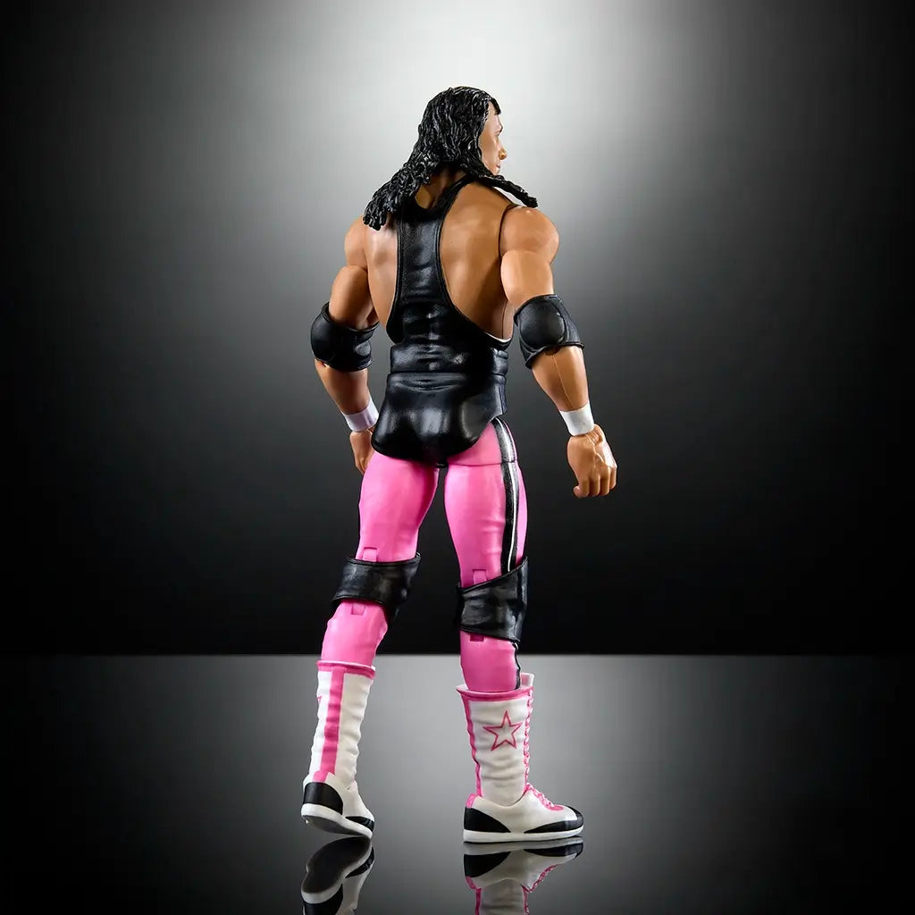 Rear angled view of WWE Elite Bret Hart action figure highlighting detailed hair sculpt, black singlet back, pink tights with side stripes, and tall white boots.