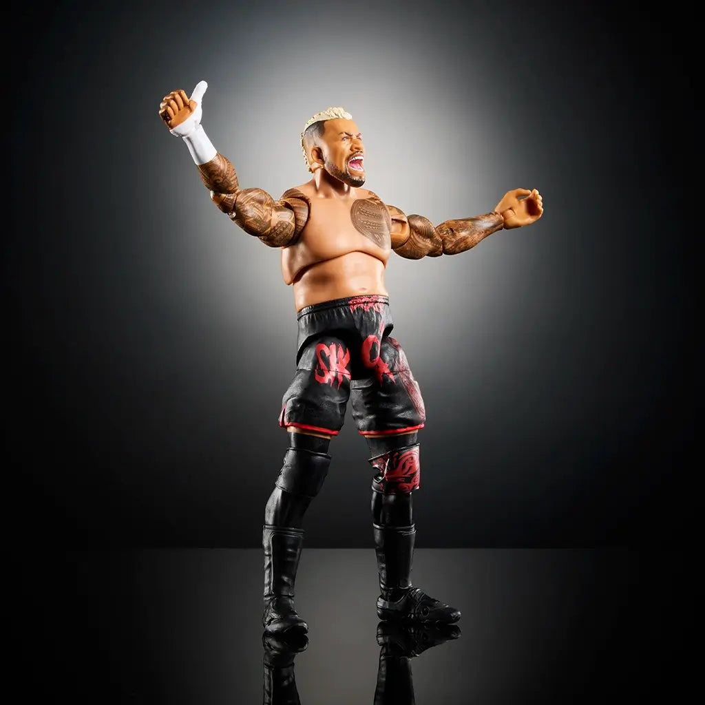 WWE Solo Sikoa action figure posed with arms raised, detailed tattoos, black shorts with red tribal graphics, knee pads, and black boots on a reflective surface.