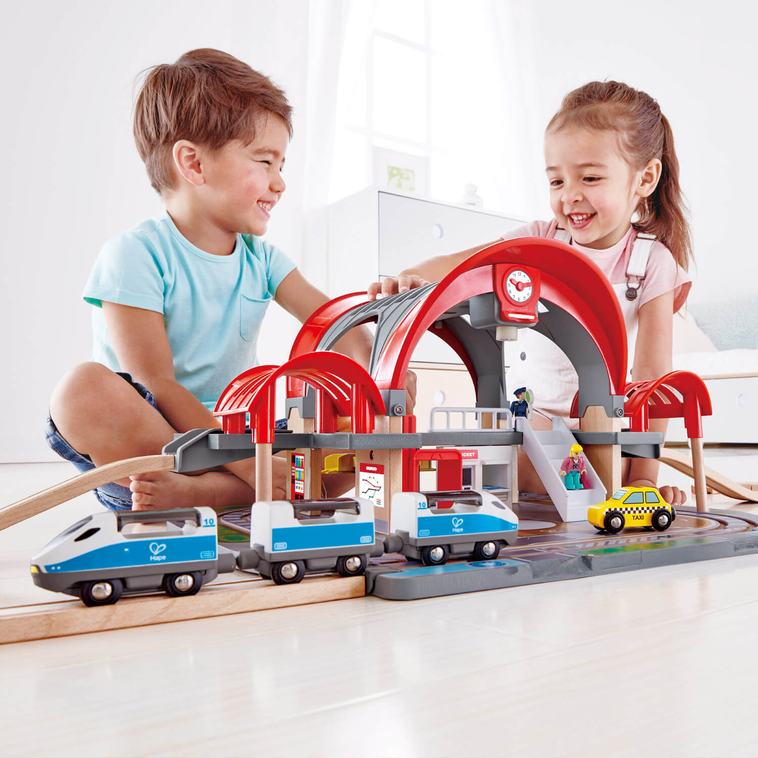 Boy and girl both play with the wooden tracks of the Hape rail grand city station.