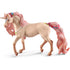 Schleich bayala unicorn mare figure features a cream textured coat, glittering pink mane and flowing tail, golden horn, blue gems, and floral decorations, posed walking on white.